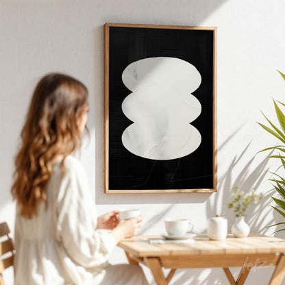 modern abstract wall art featuring white shapes on black background in a light wood frame displayed against a white wall with a plant nearby