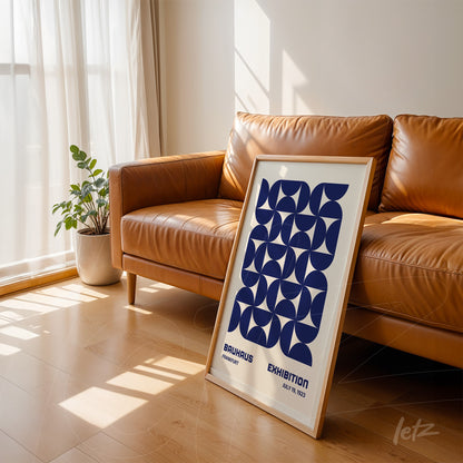 poster with navy blue geometric design in light wood frame, leaning against leather sofa in sunlit room