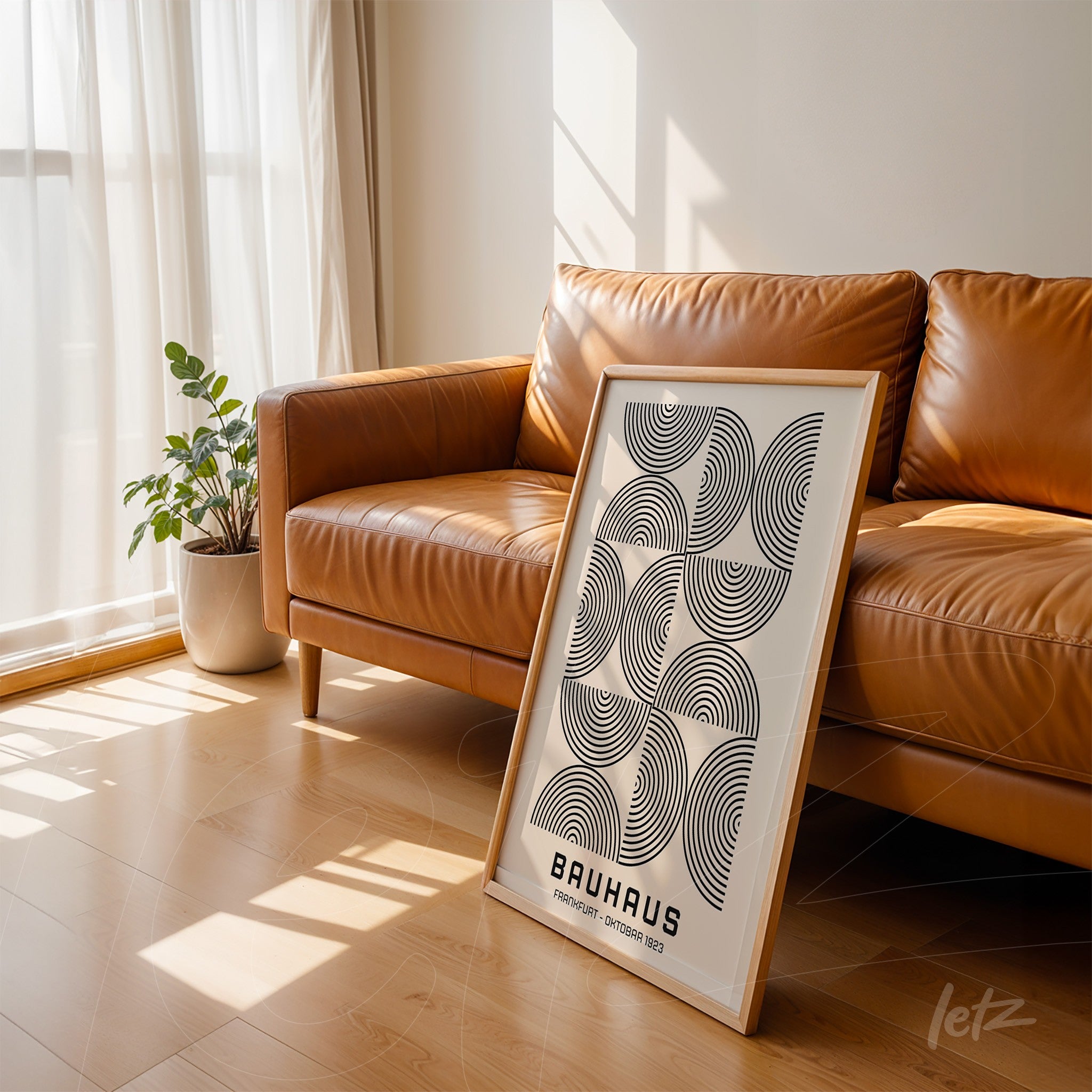 poster art with geometric Bauhaus-inspired design leaning against a brown sofa in a minimalist room with light wood flooring
