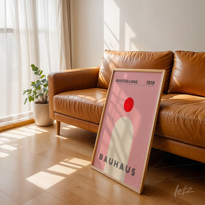poster featuring geometric Bauhaus design in light wood frame, leaning against a brown leather sofa in a well-lit setting