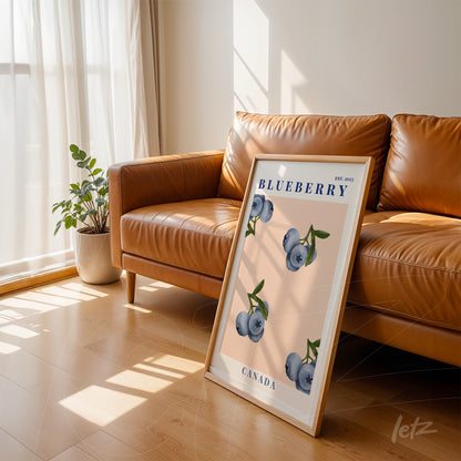 framed wall art featuring minimalist illustration of blueberries with blue text, leaning against orange leather sofa