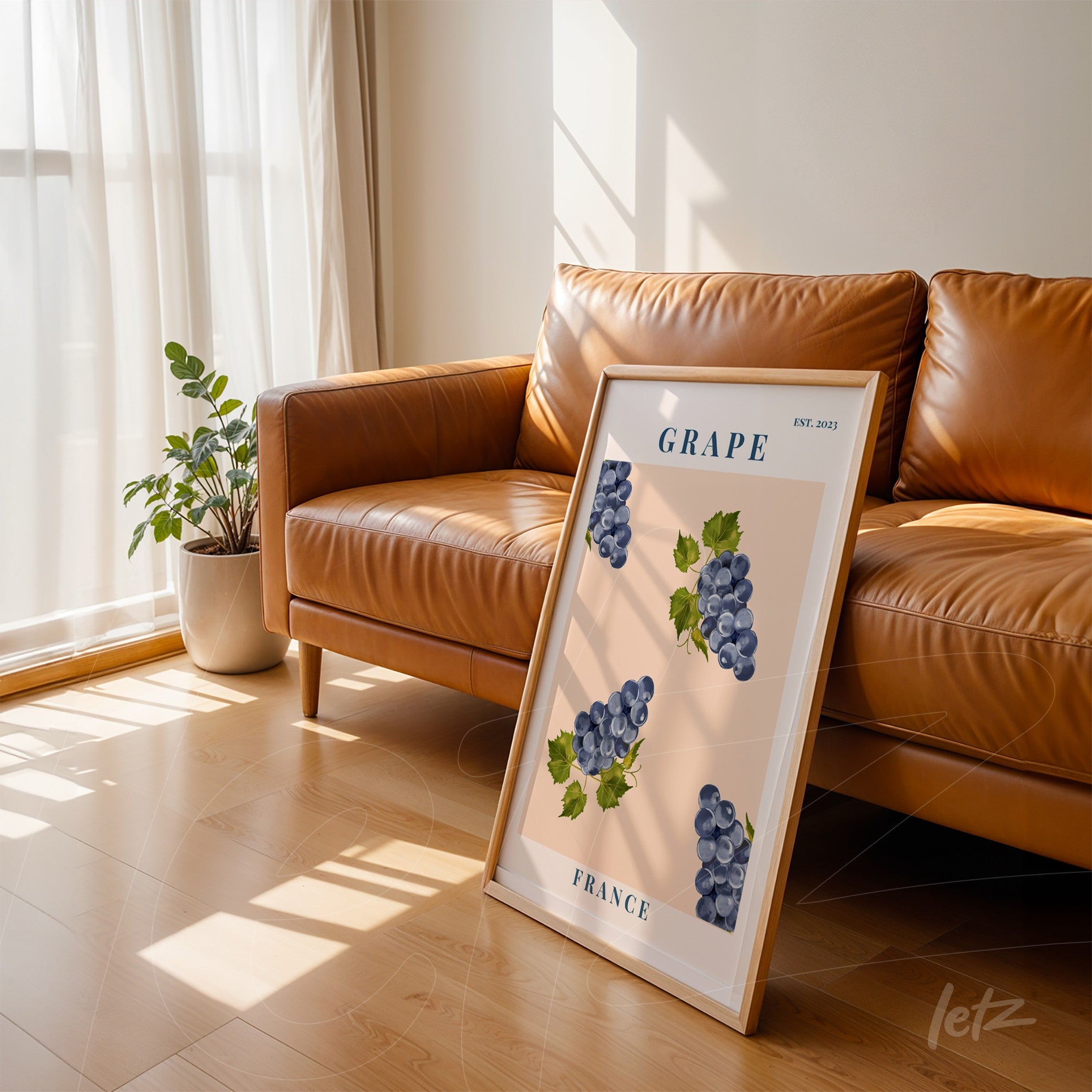 decorative wall art featuring bunches of purple grapes on a light pink background with a light wood frame leaning next to a caramel leather sofa