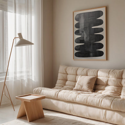 abstract framed wall art featuring oval shapes in black tones, displayed in a minimalistic living room with a beige sofa and light wood side table