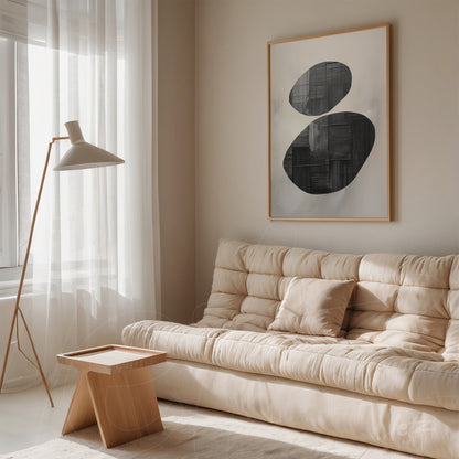 framed abstract artwork in black and white with light wooden frame hanging beside a beige sofa