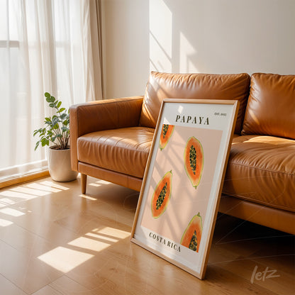 framed art of papayas in white frame leaning against caramel leather sofa with natural light