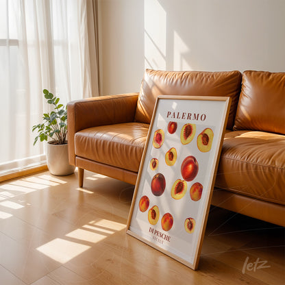 framed art featuring various peaches in light wooden frame leaning against brown sofa with bright window background