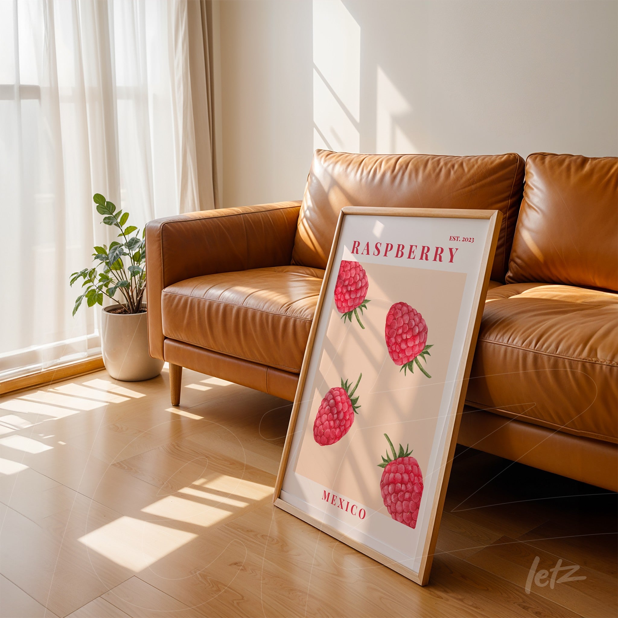 framed art print featuring raspberries in light frame leaning against brown leather sofa with plant in the background