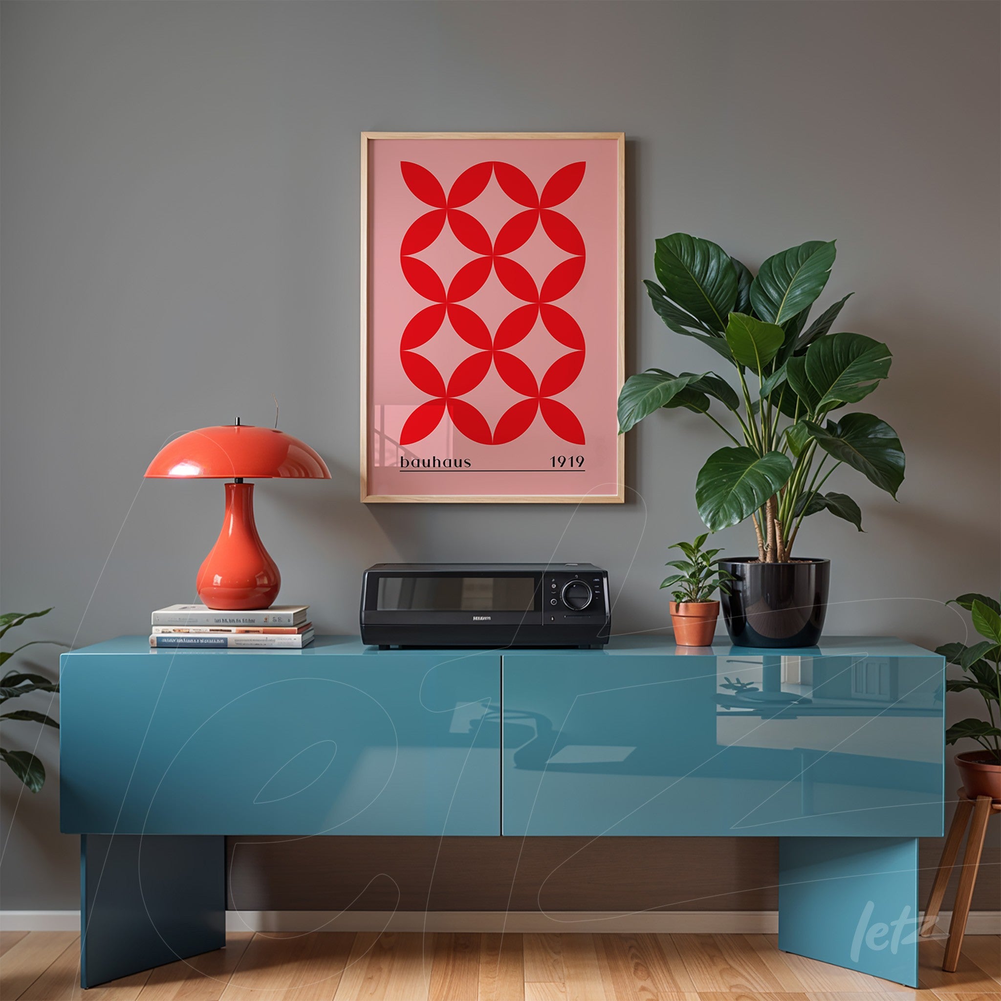 poster with red geometric art and text 'bauhaus 1919' in a light wood frame on gray wall, displayed on a glossy blue sideboard with red lamp and plants