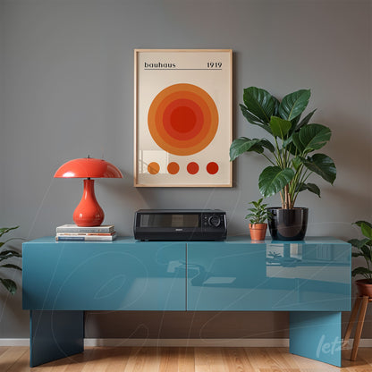 poster featuring concentric circles in shades of orange and red framed above blue sideboard with vintage lamp and plants