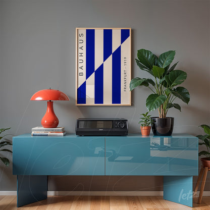 poster in light frame featuring geometric blue and white art, displayed above a blue sideboard with a red lamp and plant