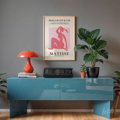 decorative art print by Matisse in light frame displayed above a blue sideboard, surrounded by plants and a red lamp
