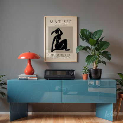 decorative wall art featuring a black silhouette of a woman in light frame, displayed in a modern setting with a blue table and plants in the background
