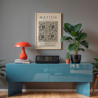 framed art print of Matisse's work in beige frame above a modern blue sideboard, featuring greenery and an orange lamp