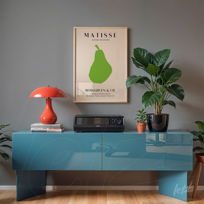 framed modernist artwork of a green pear displayed above a blue wooden console in a cozy indoor setting with plants