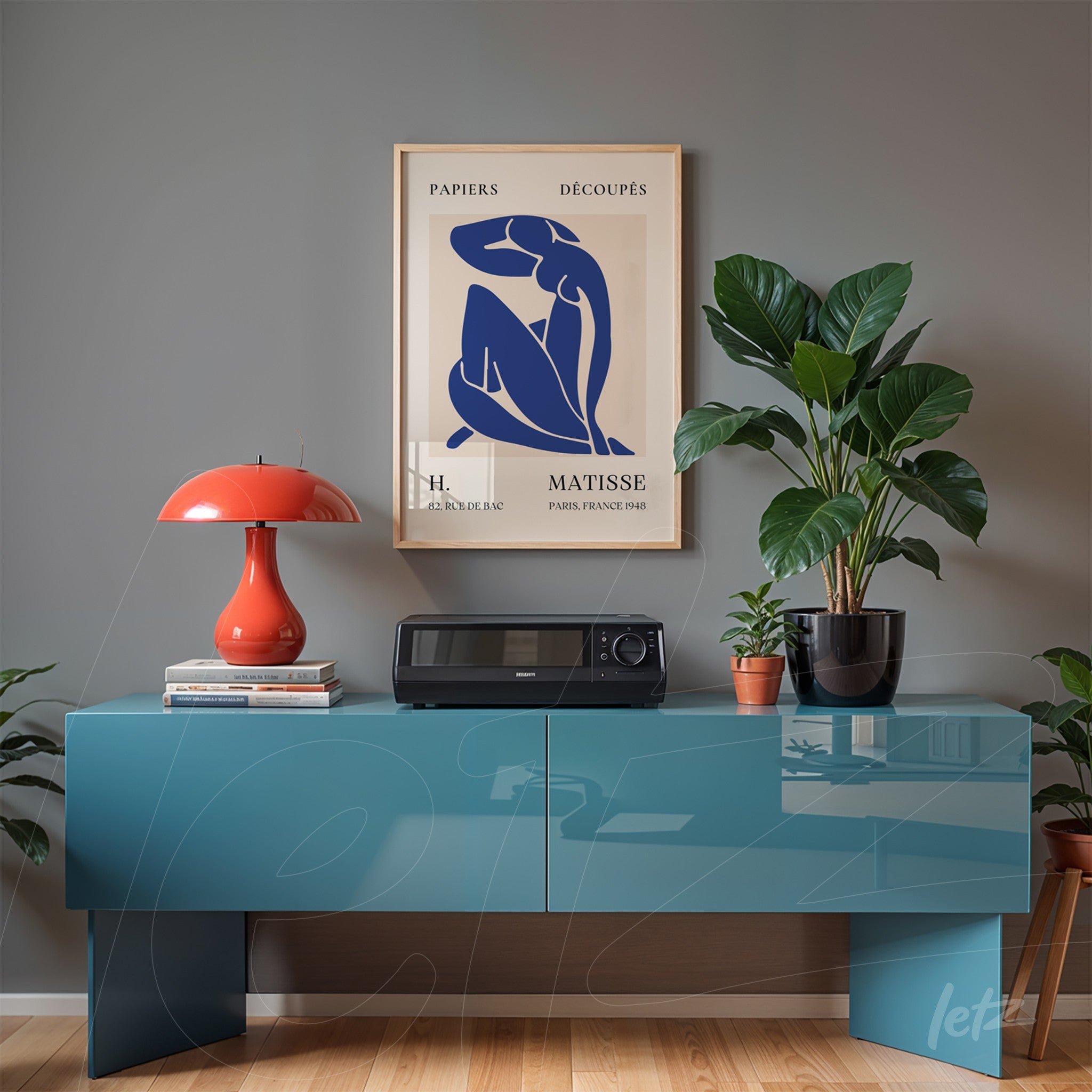 framed modern art of female figure in light frame displayed on blue console in a space with plants