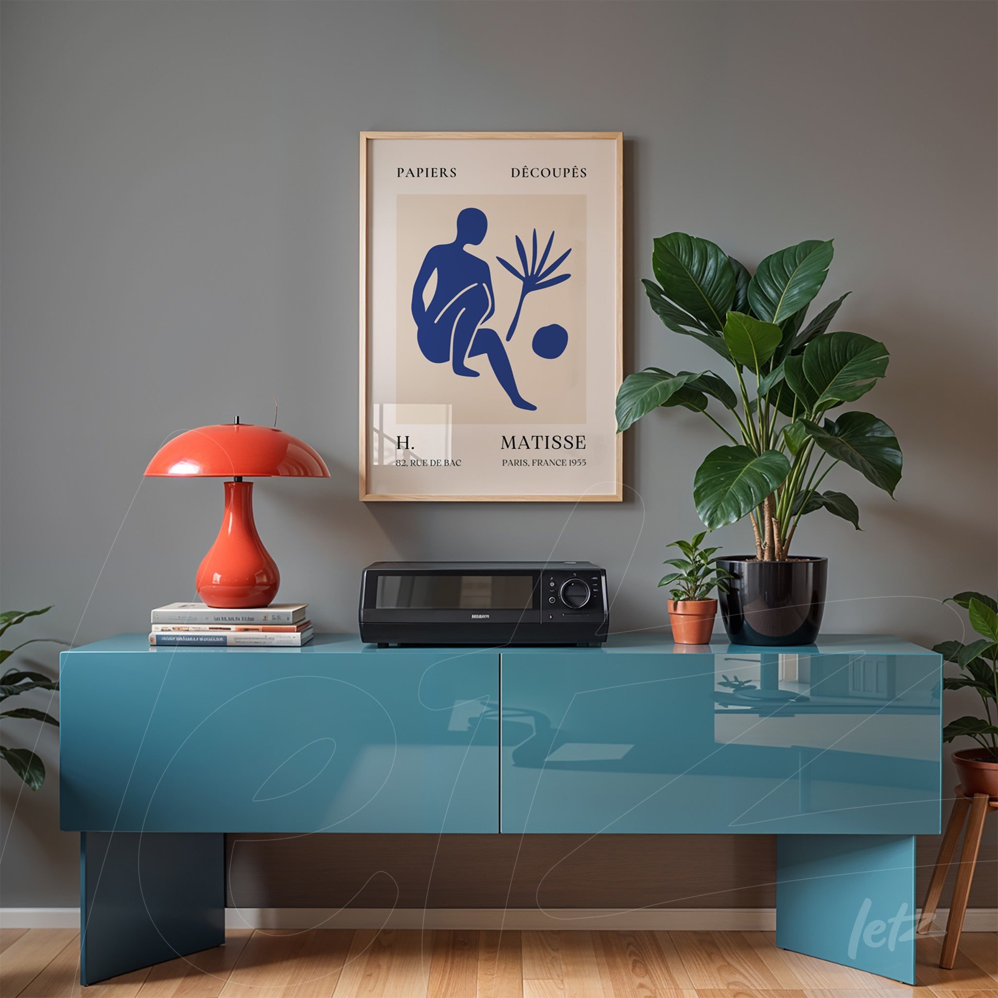 framed art piece by Henri Matisse displayed above a blue sideboard with orange table lamp and black potted plant beside it