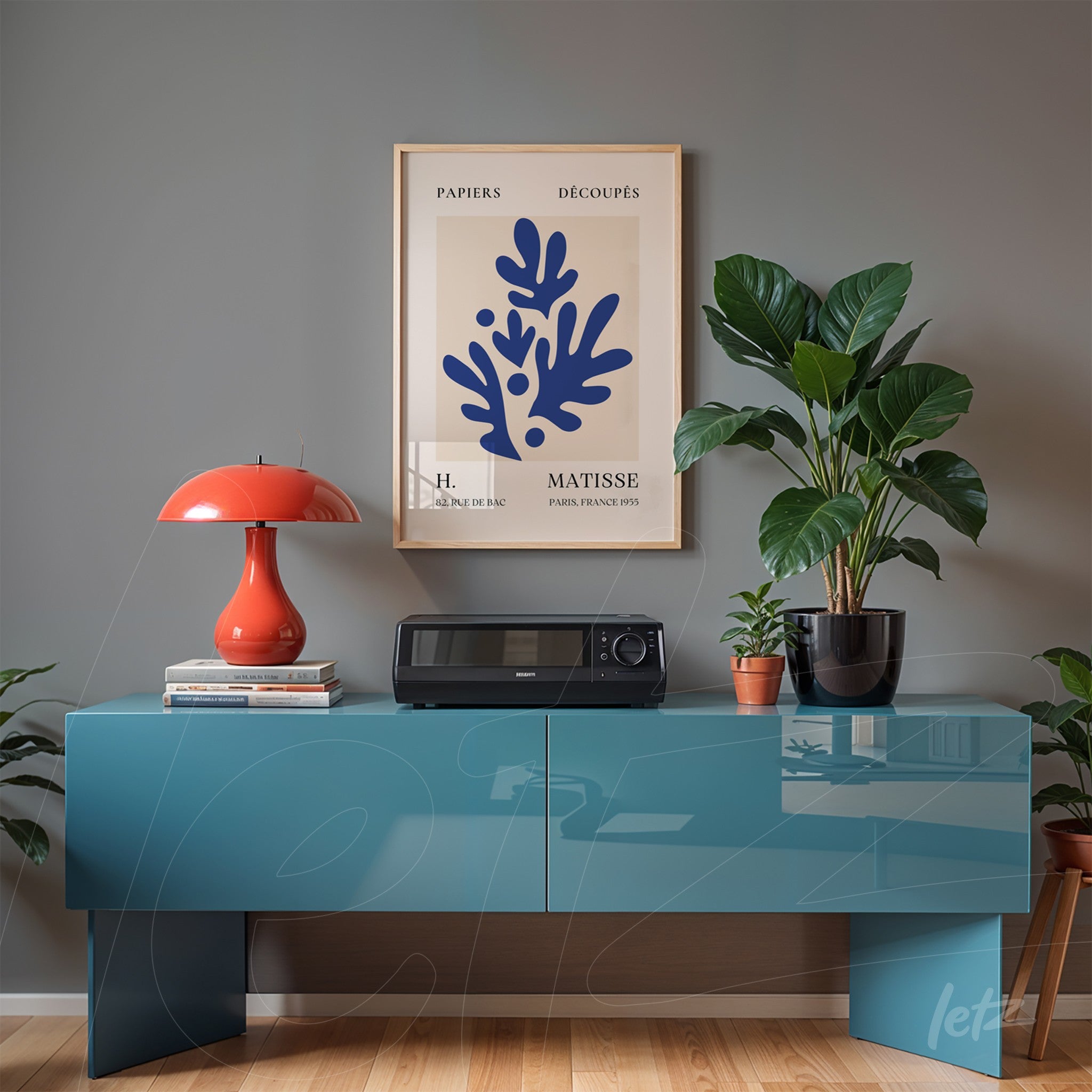framed wall art featuring blue paper cutouts by Henri Matisse displayed above a modern blue cabinet with plants nearby