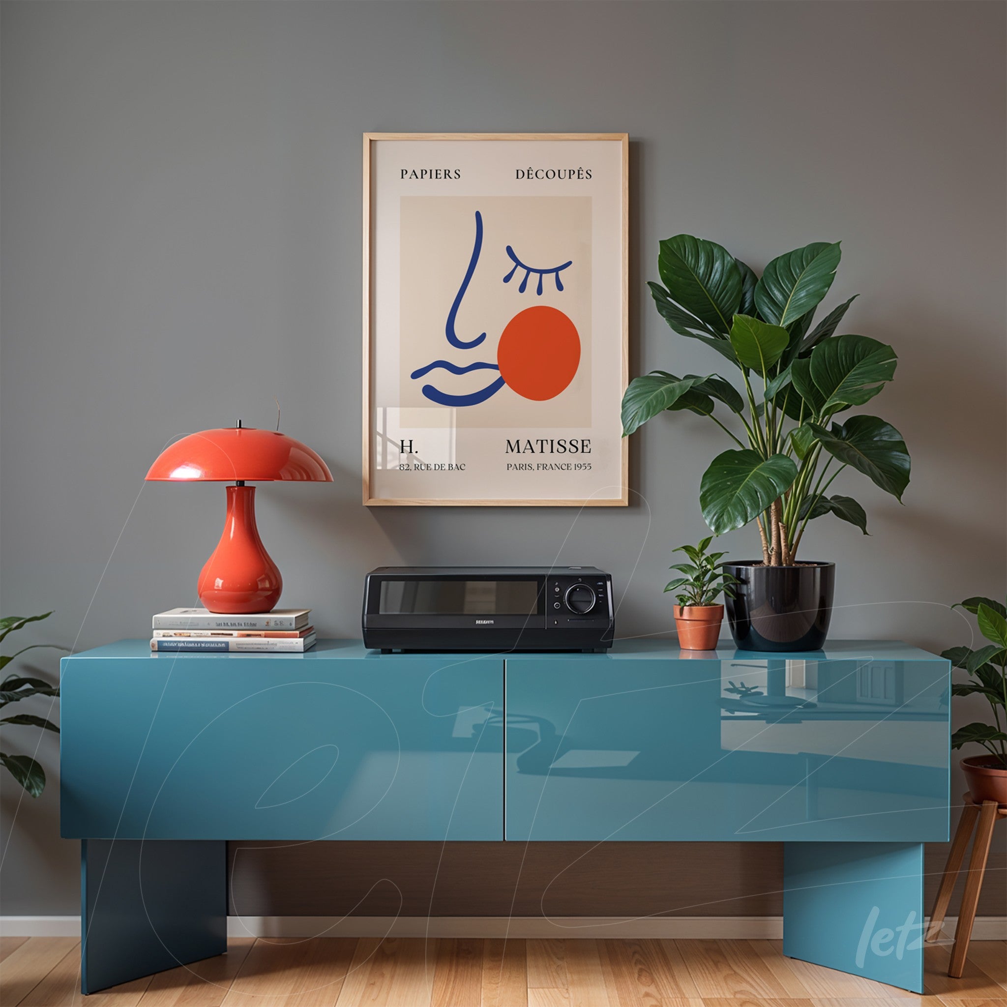 framed wall art in gold frame featuring a minimalist illustration of a face with red accents displayed on a blue table with a potted plant beside it