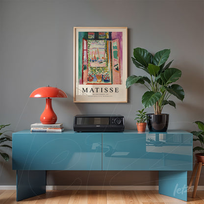 vintage artwork of a landscape by Matisse in a light frame above a blue sideboard, decorated with a red lamp and green plants