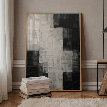 abstract artwork in black and white with light wooden frame leaning against a wooden table beside a stack of books