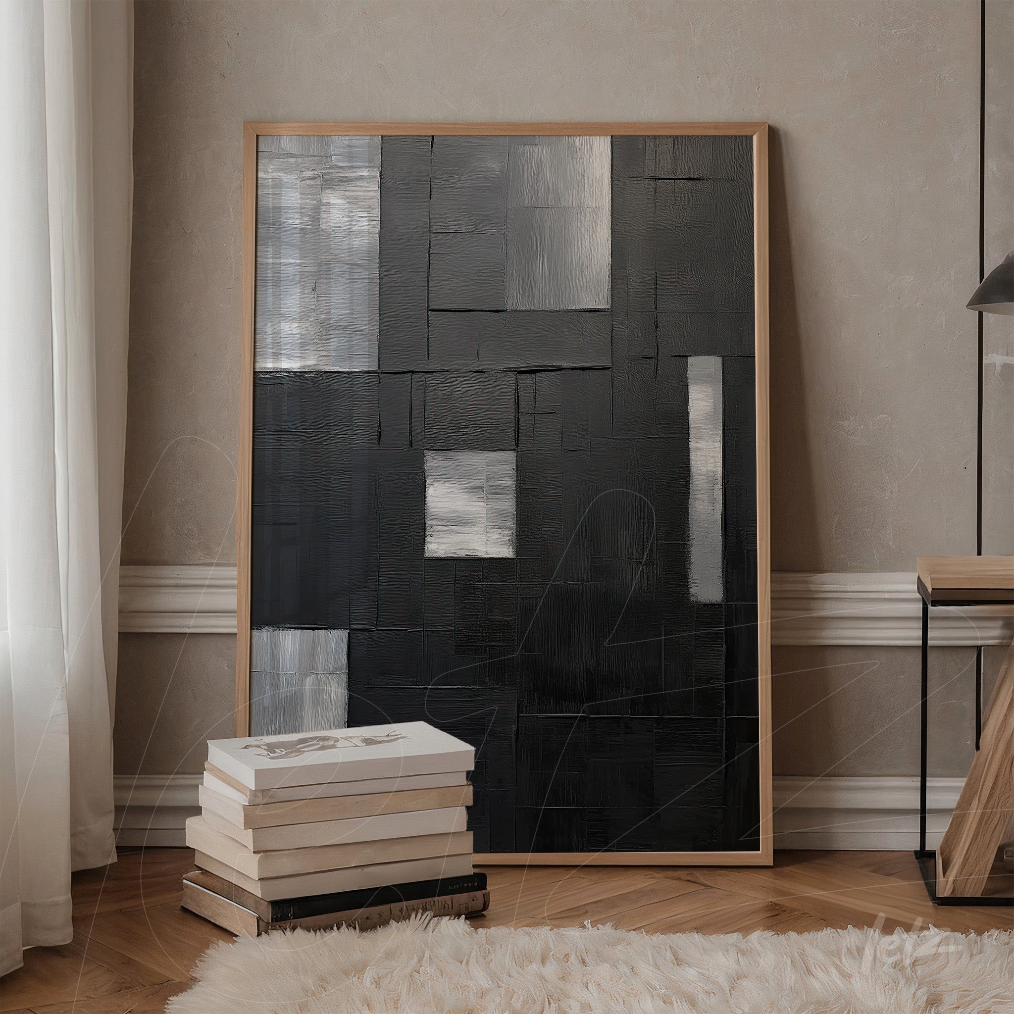 canvas artwork featuring abstract design in shades of black and gray, framed in light wood, displayed on a table beside a stack of books
