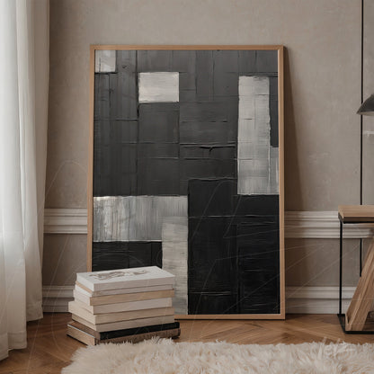contemporary artwork featuring black, gray, and silver textures in a light wood frame displayed against a beige wall