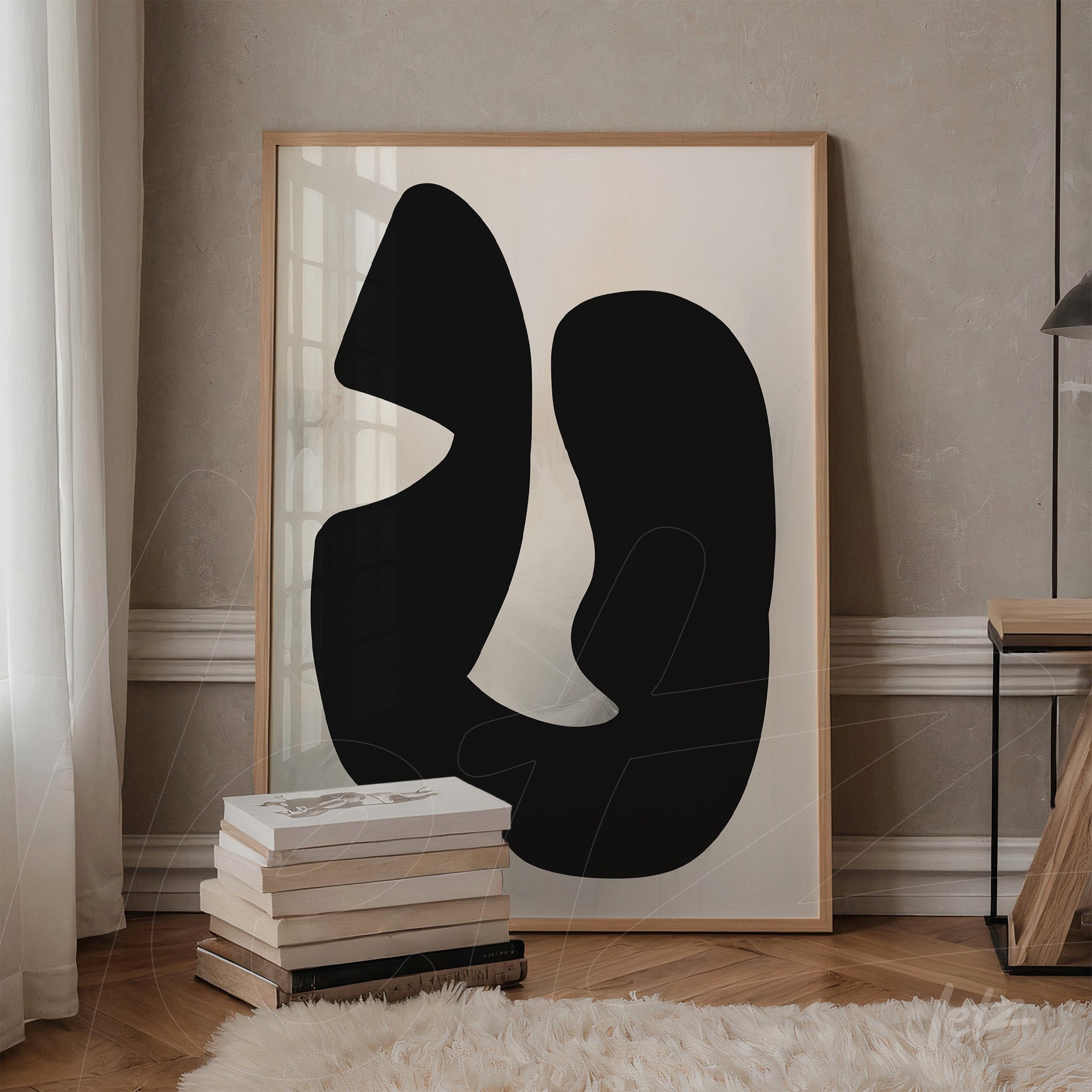 abstract black and white artwork featuring fluid shapes in a light wood frame, leaning against a stack of books in a minimalist setting