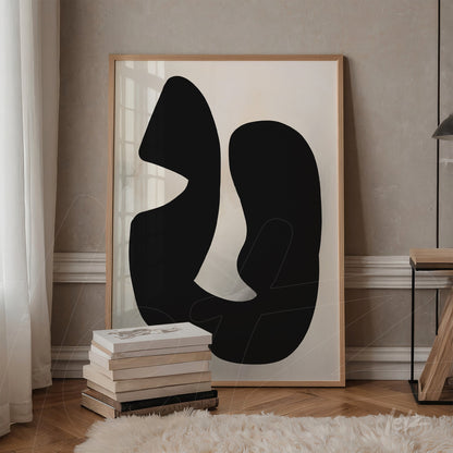 abstract black and white artwork featuring fluid shapes in a light wood frame, leaning against a stack of books in a minimalist setting