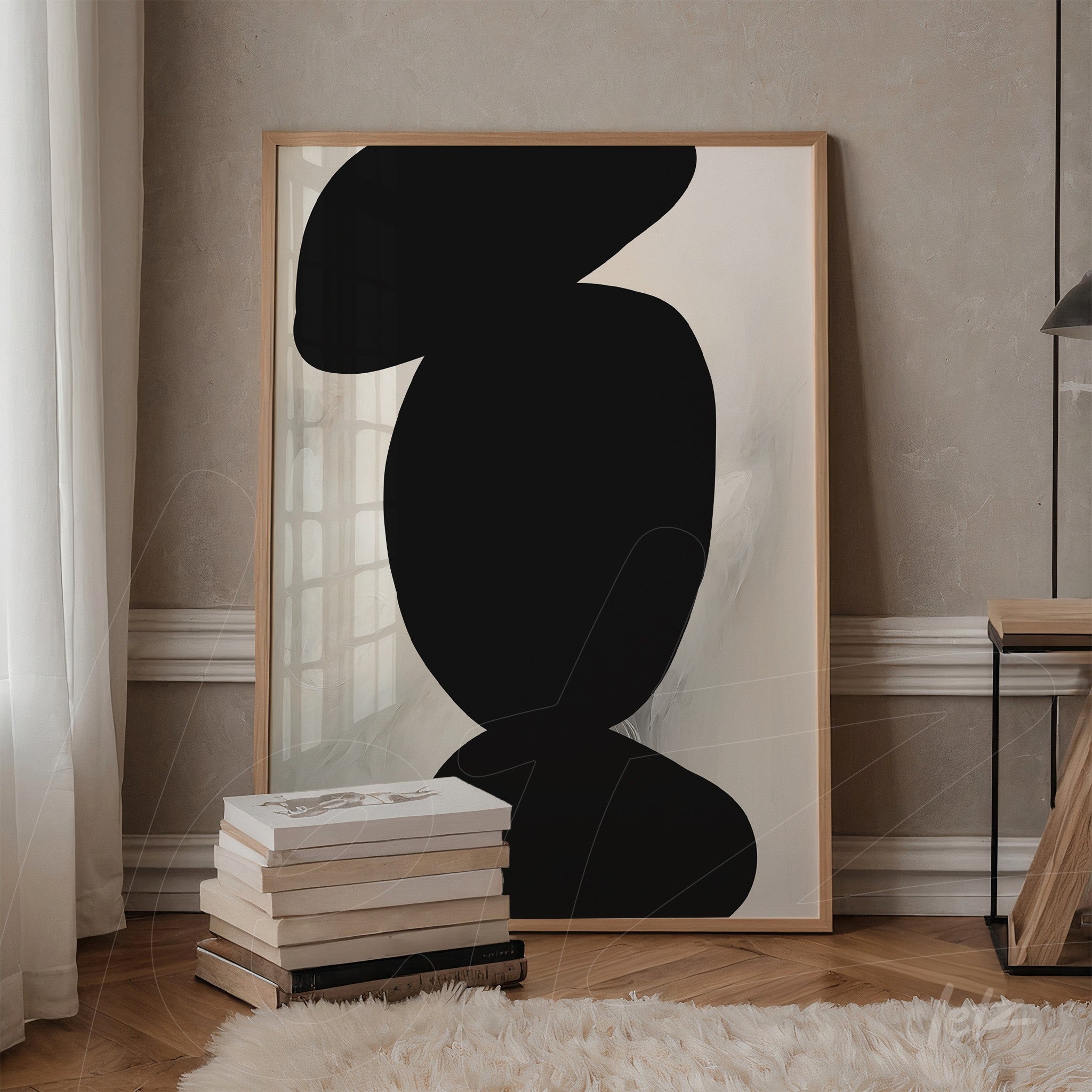 abstract artwork featuring black shapes on a light background, framed in light wood, leaning against a table next to a stack of books