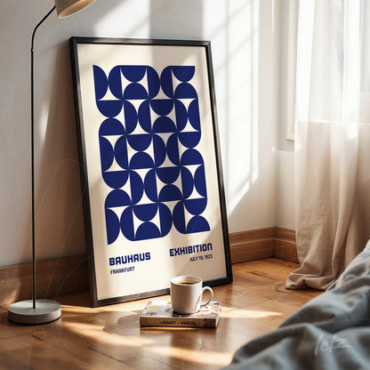framed poster with blue geometric Bauhaus-inspired art, leaning against white wall near floor lamp