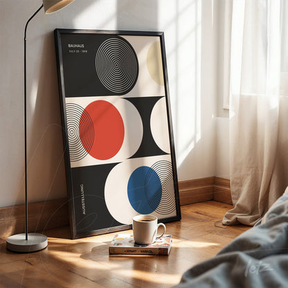 framed geometric bauhaus style art print propped on wooden floor, featuring colorful circles on black and white background, next to a modern lamp