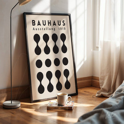 bauhaus style artwork with black geometric shapes on cream background in black frame, displayed on wooden floor with natural light