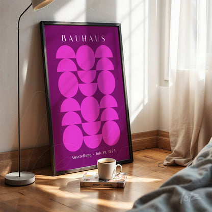 poster print with geometric pink design in a black frame leaning on a wooden floor near a window