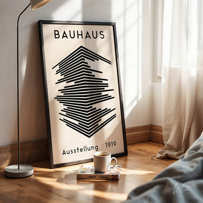 printed poster with geometric Bauhaus-inspired design in black frame leaning against white wall next to a lamp