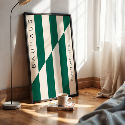 printed poster featuring geometric design with green and white stripes in a black frame, resting on a wooden floor near a sunlit window