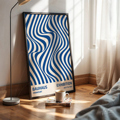 poster featuring geometric blue and white illustration with black frame leaning on the floor in a sunlit room