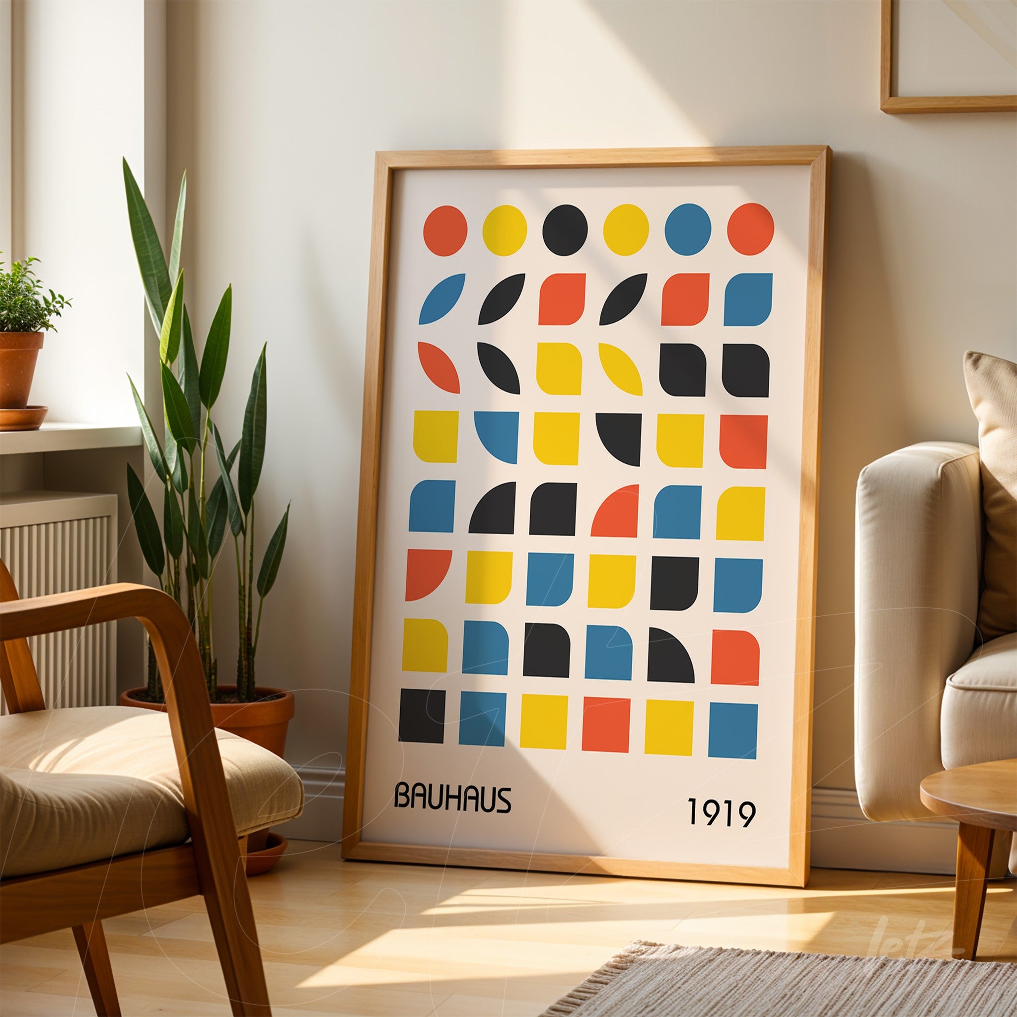 poster with geometric Bauhaus style design in a light wooden frame, leaning against the floor near a sofa and decorative plant