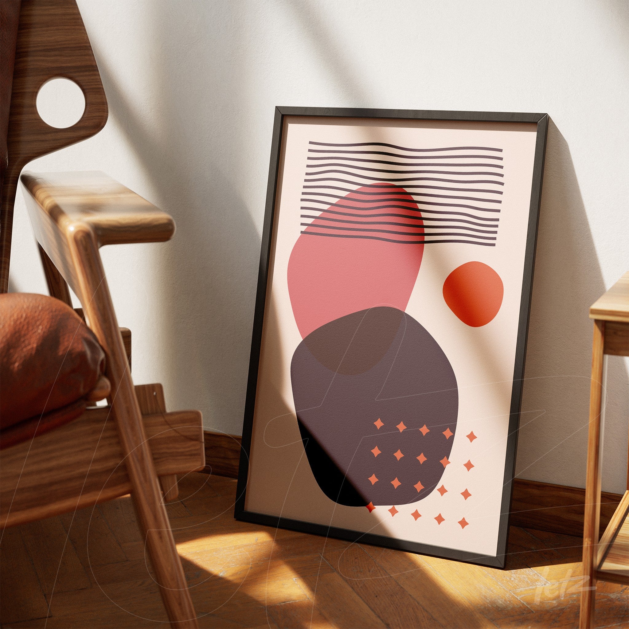 abstract poster with pink, orange, and black shapes in slim black frame leaning against a light wall