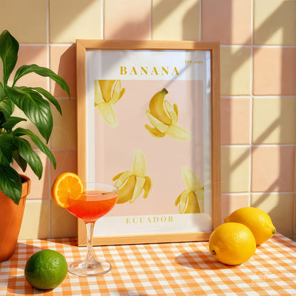 framed art print of stylized bananas in light wooden frame against a beige background with fruits and a vibrant cocktail