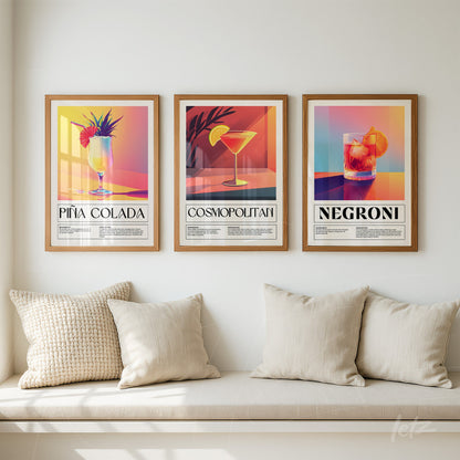 series of framed artworks featuring colorful cocktail illustrations of piña colada, cosmopolitan, and negroni in light wood frames