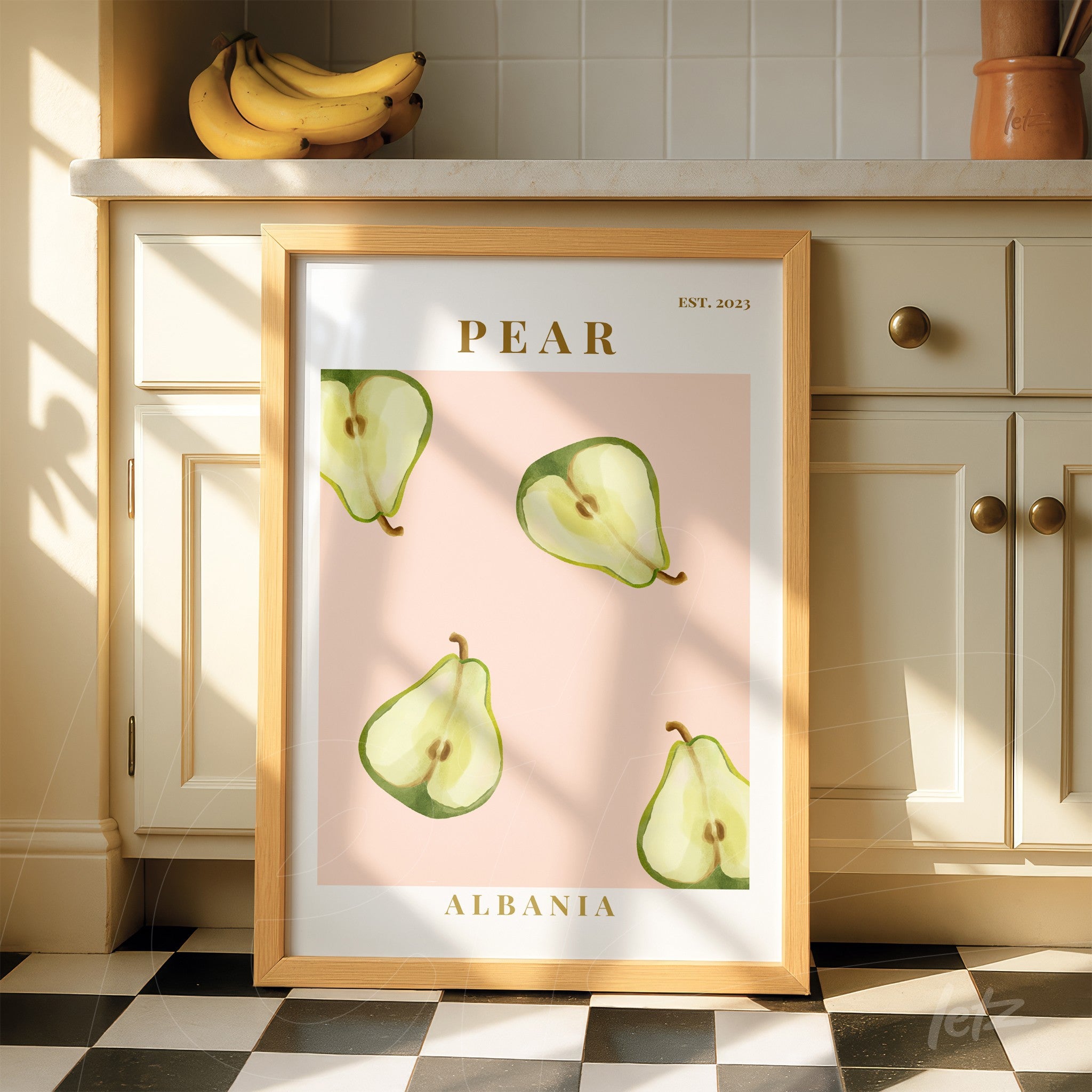 framed wall art featuring green pears on pink background with light wood frame and golden text
