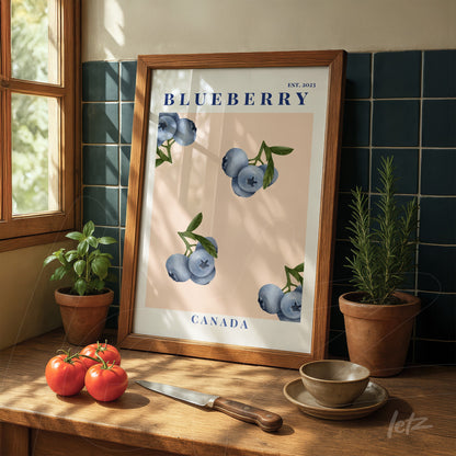 framed wall art featuring blueberry illustration on pink background displayed in a kitchen with a plant beside