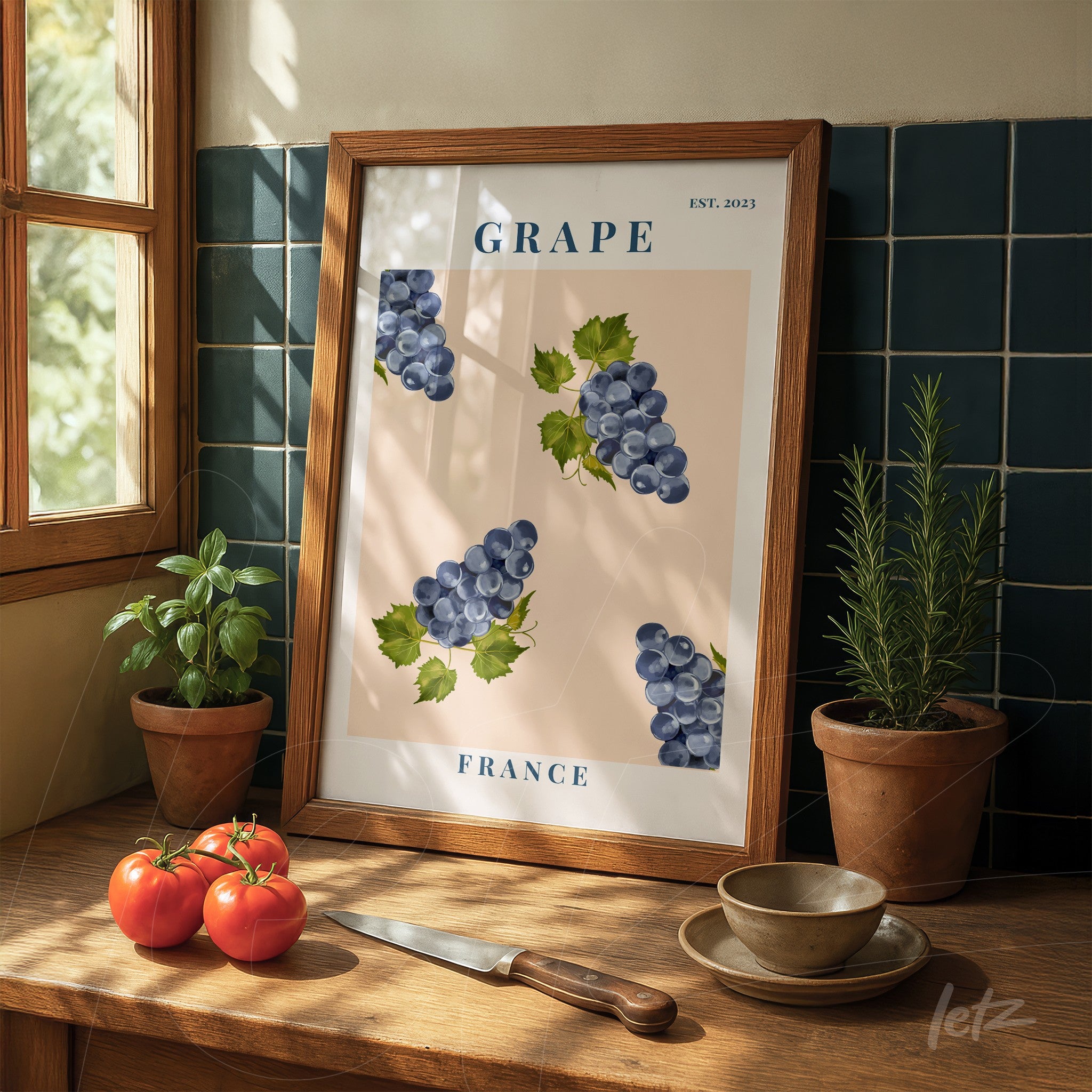 decorative wall art featuring an illustration of grapes on a light background, wooden frame, displayed on a wooden table with tomatoes and herbs