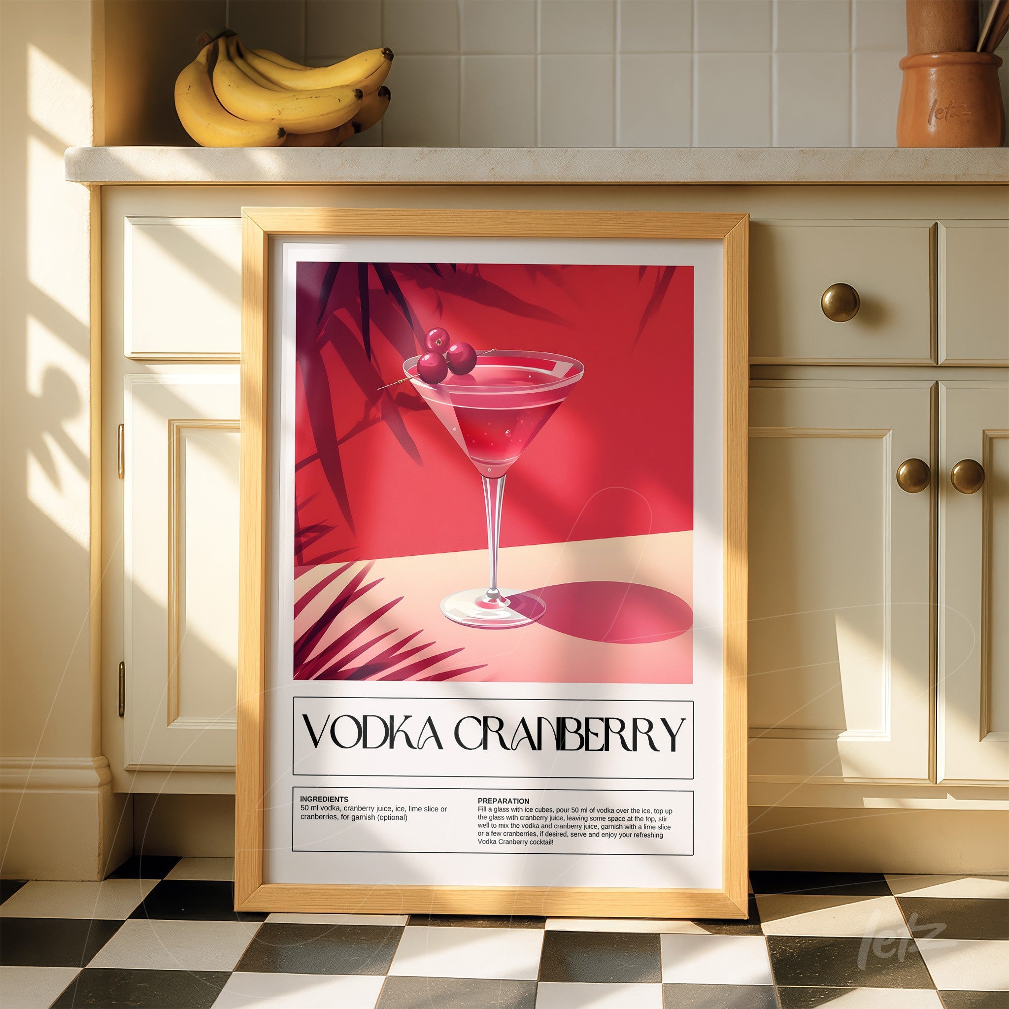 framed retro artwork of vodka cranberry cocktail displayed with a red background and leaf details, propped against a light kitchen surface