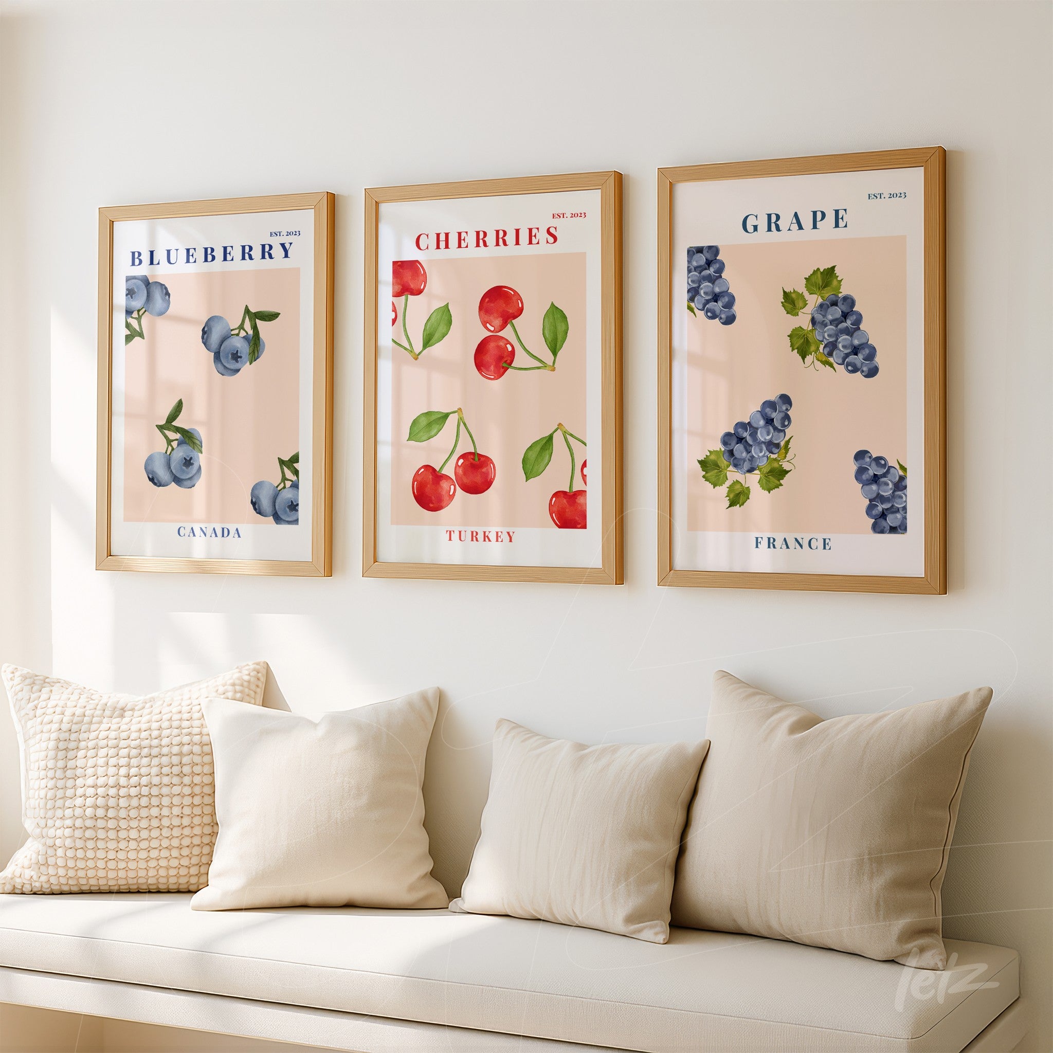 decorative wall art collection featuring blueberries, cherries, and grapes in light wood frames displayed on a neutral wall with light-colored pillows in the foreground