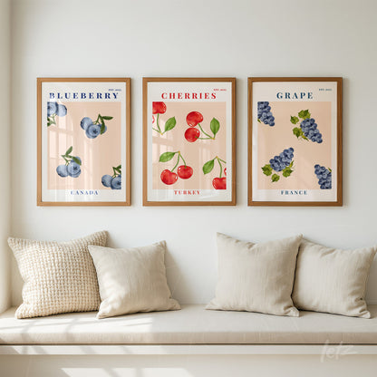 composition of framed wall art featuring blueberries, cherries, and grapes with light wood frames against a soft pink background