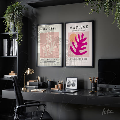 collection of two framed modern art prints with black frames, one featuring a pink background with abstract foliage in pink and the other showcasing a beige background with red foliage detail, displayed in a stylish office setting with dark shelves