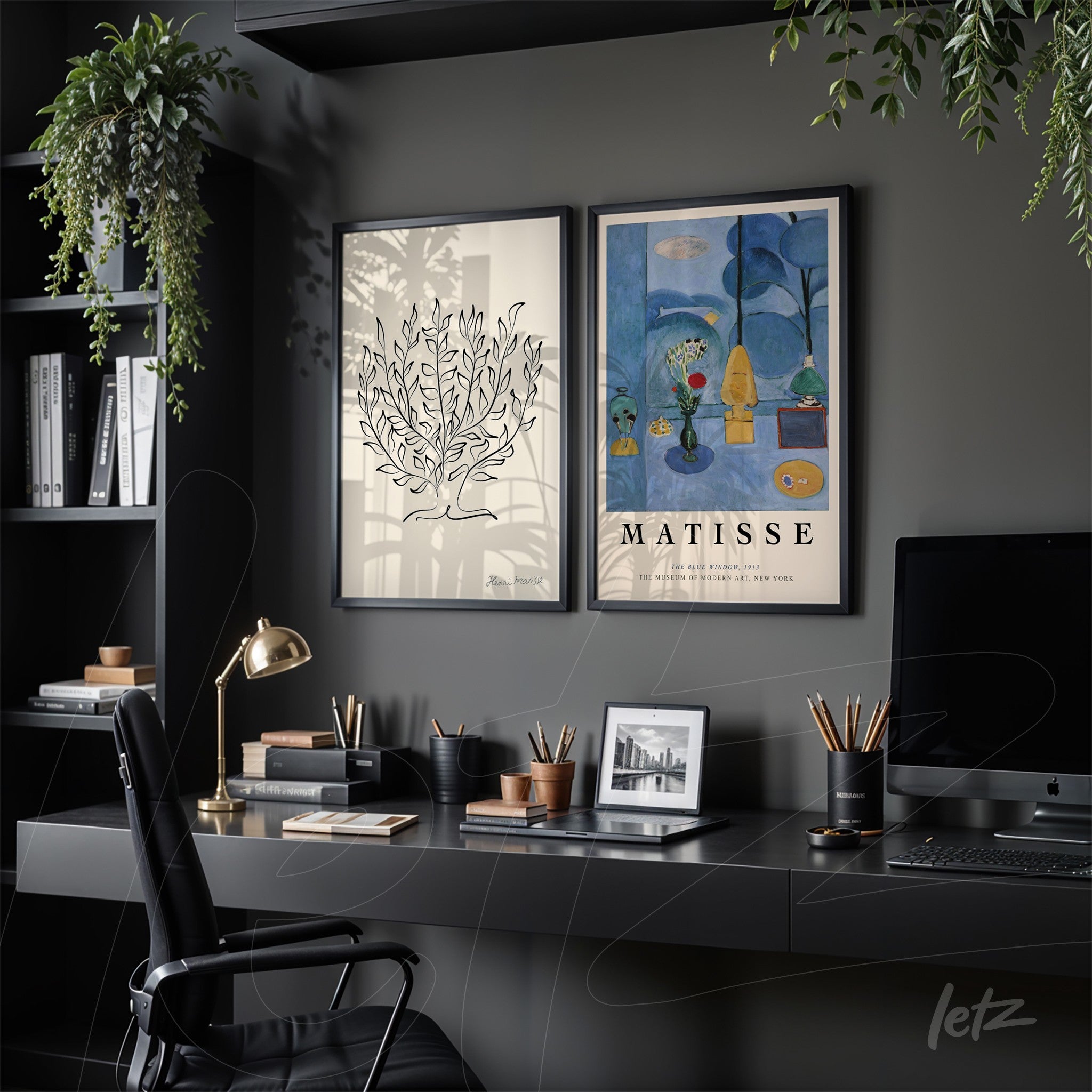 arrangement of two framed artworks on a workspace, one featuring minimalistic plant design and the other a colorful illustration by Matisse, both in deep black frames against a dark gray wall