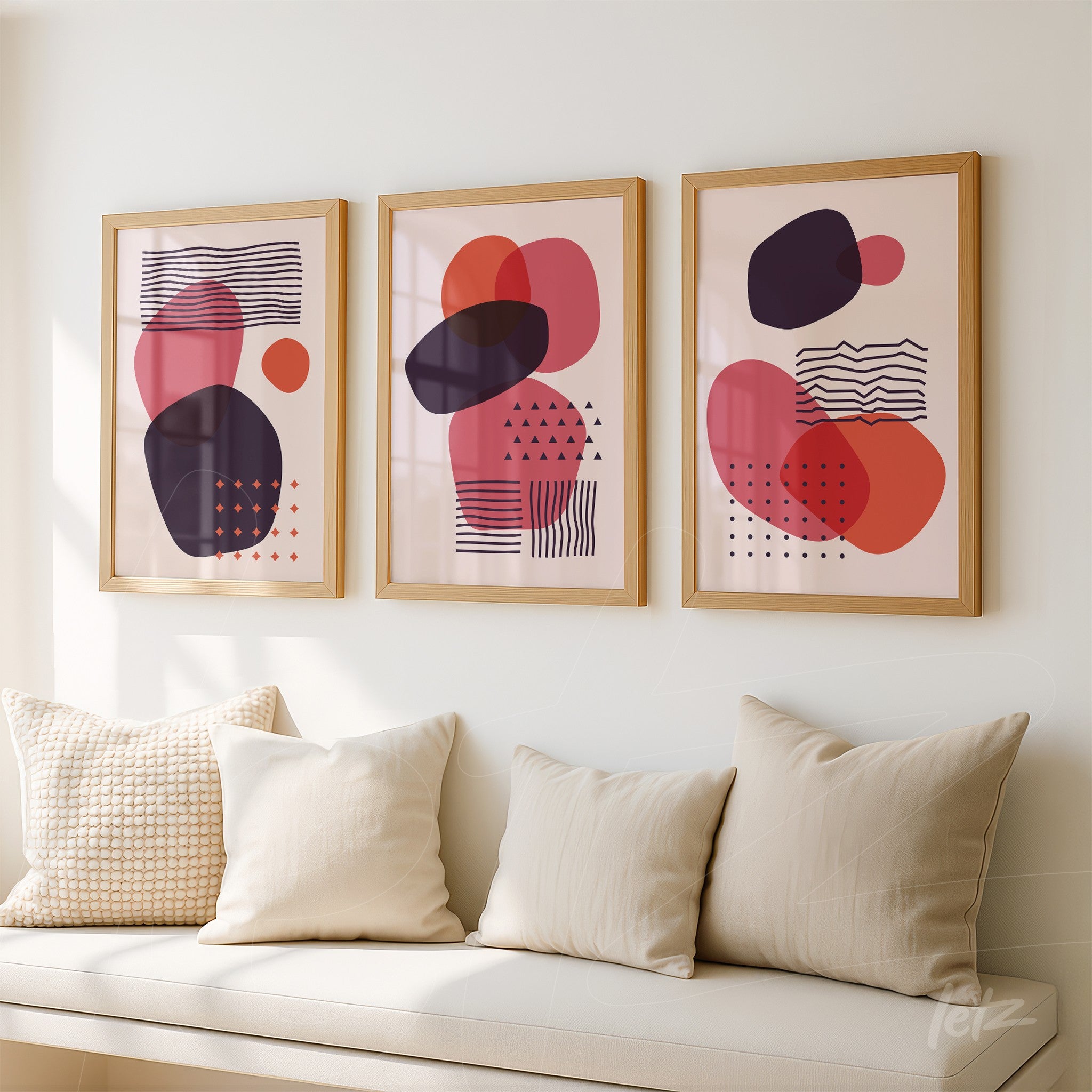 set of three abstract art prints in shades of pink, red, and black with light wood frames on white wall in living room