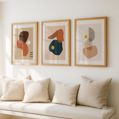 set of three abstract prints in light wooden frames displayed on a white wall above a cushioned bench